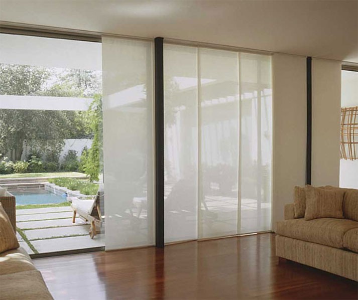 Persiana panel japonés colocada en gran ventanal ayudando a separar el interior de una sala y el exterior de un patio con piscina.
