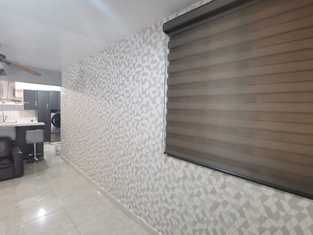 Papel tapiz color gris de formas geometricas triangulares, colocado en pared con ventana con persiana sheer elegance.